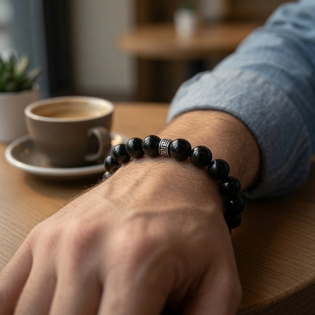 Close-up of natural black obsidian bracelet showing mirror-smooth jet-black bead surface with vitreous glass-like luster and sterling silver engraved key-pattern accent bead