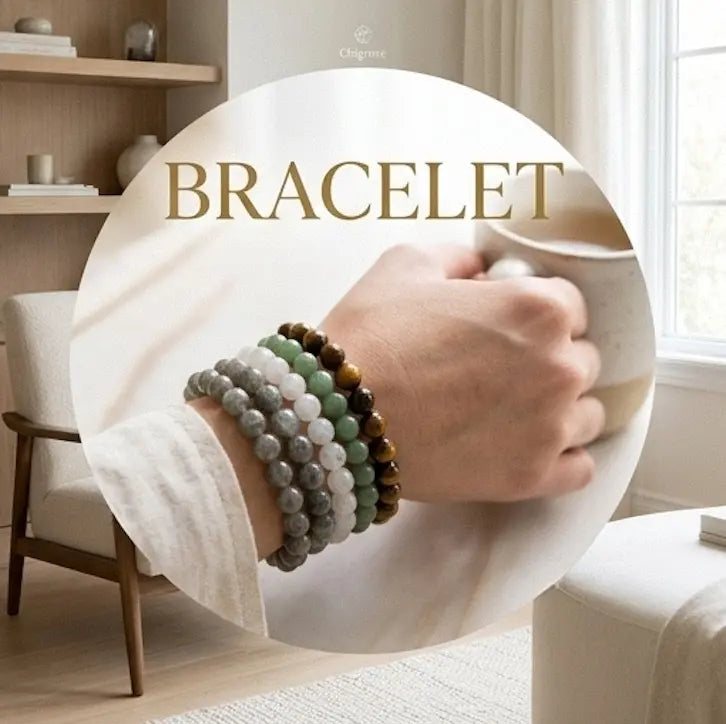 Woman wearing stacked natural crystal bracelets including labradorite, white moonstone, green aventurine, and tiger's eye beaded bracelets, holding a ceramic mug in a warm minimalist interior