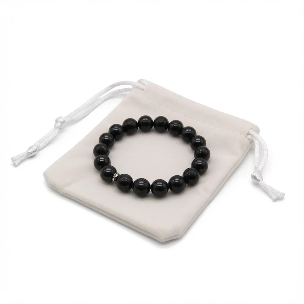 Black obsidian bracelet placed on dark cloth beside sage bundle and candle for energetic cleansing ritual, protection stone smudging and intention setting practice