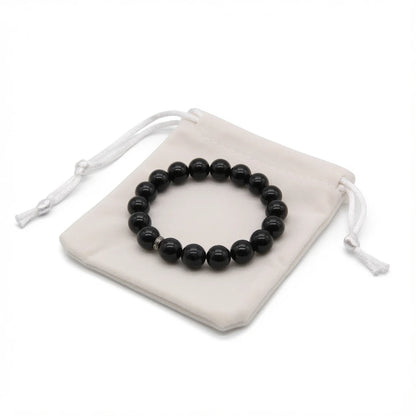 Black obsidian bracelet placed on dark cloth beside sage bundle and candle for energetic cleansing ritual, protection stone smudging and intention setting practice