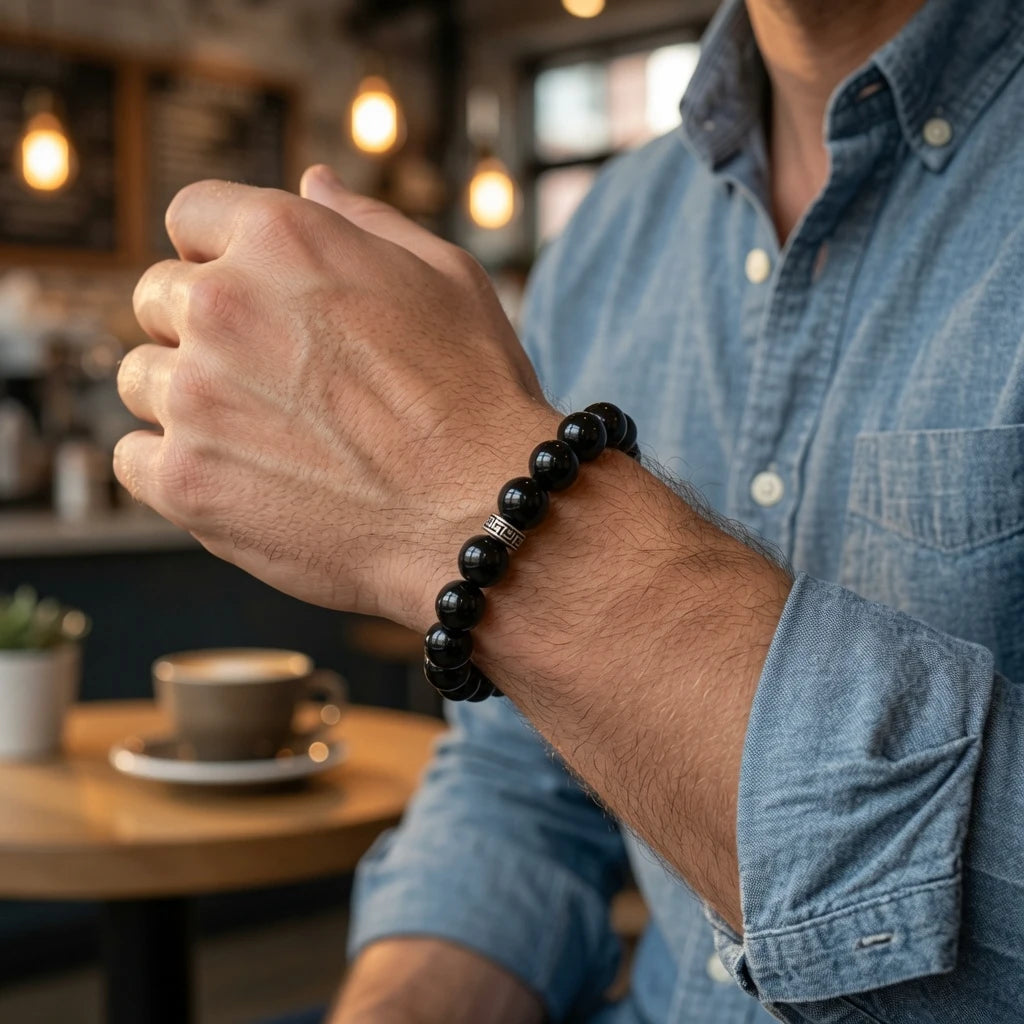 Person wearing black obsidian bracelet on left wrist showing deep glossy volcanic glass beads against skin in natural daylight, root chakra protection jewelry