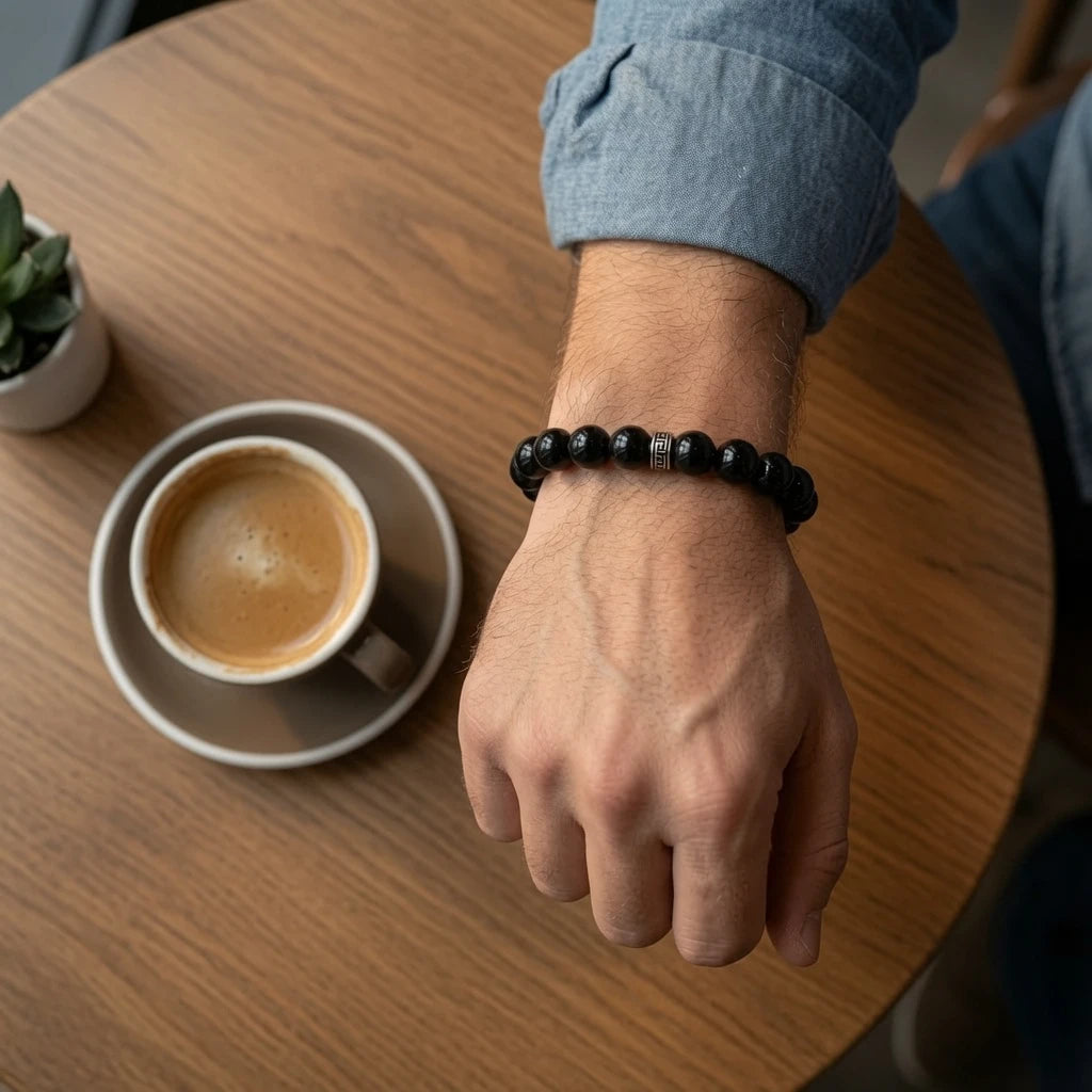 Person wearing black obsidian bracelet on left wrist showing deep glossy volcanic glass beads against skin in natural daylight, root chakra protection jewelry