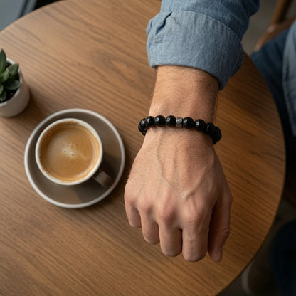 Person wearing black obsidian bracelet on left wrist showing deep glossy volcanic glass beads against skin in natural daylight, root chakra protection jewelry