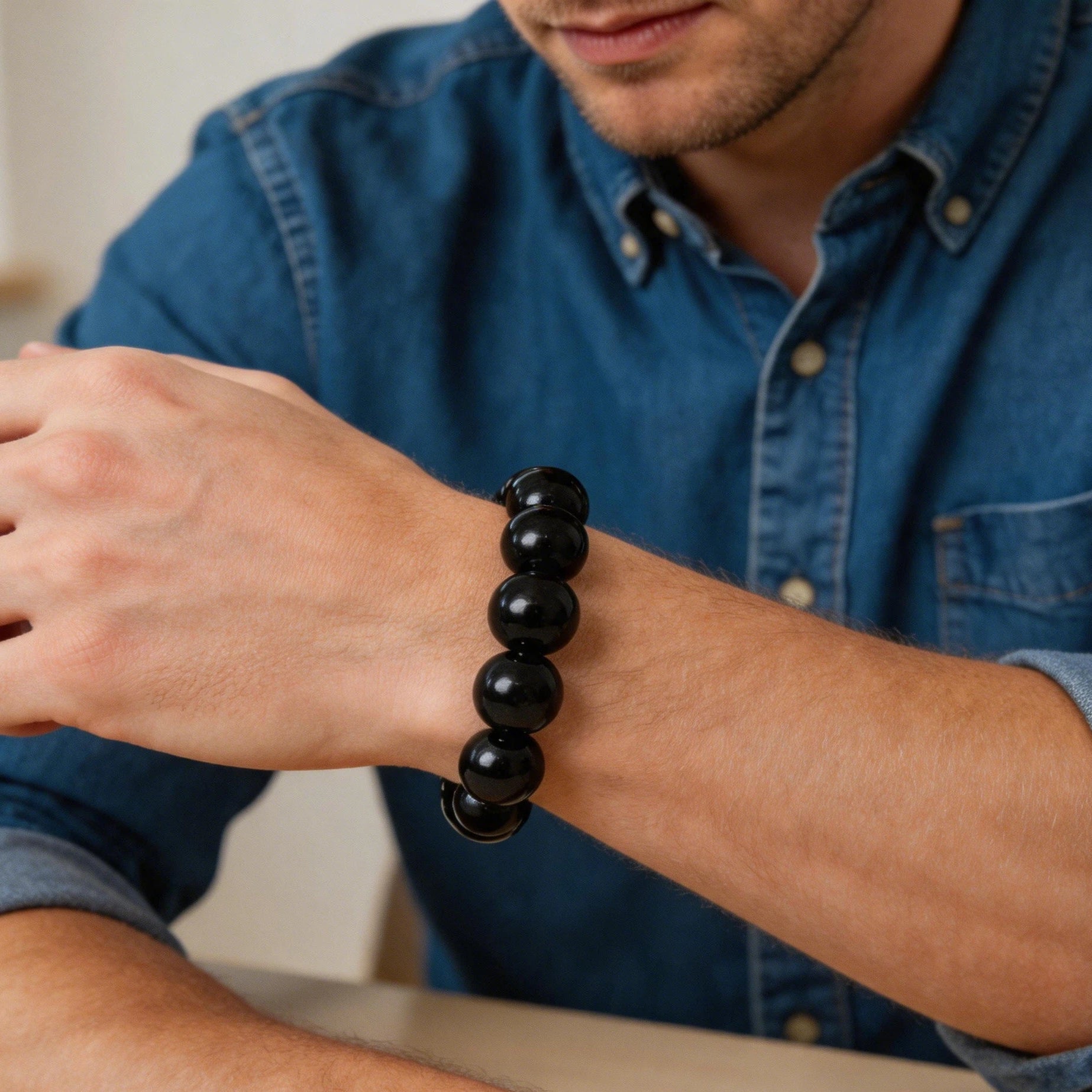 Person wearing large natural black tourmaline bracelet on wrist showing deep polished black beads against skin in natural daylight, root chakra protection jewelry