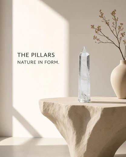 Clear quartz crystal tower on a stone table with “The Pillars” brand text