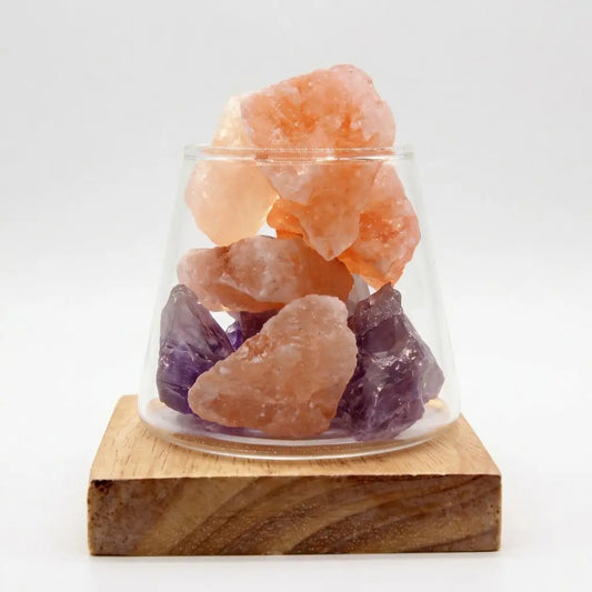 Raw Himalayan salt and amethyst crystal essential oil diffuser in clear glass vessel on natural wood LED base, warm night light glow, white background