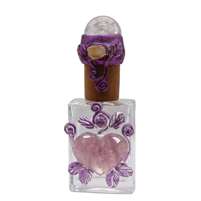 Handcrafted clear glass perfume bottle with rose quartz heart center, purple wire-wrapped leaf decoration, clear quartz sphere stopper and natural cork, healing ritual vessel on white background