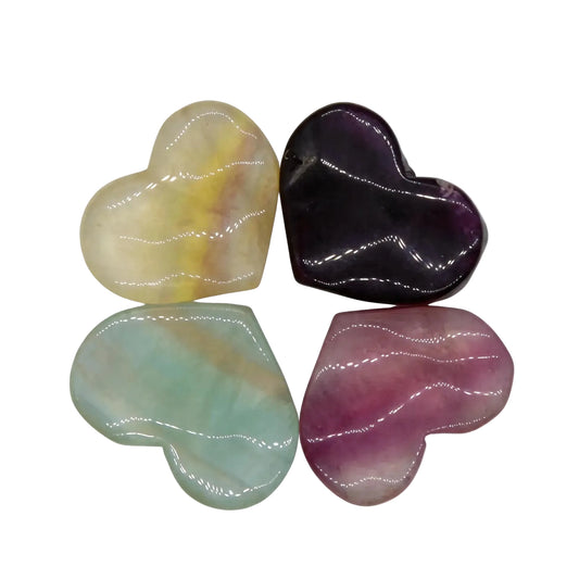 Set of four polished natural fluorite crystal hearts in yellow-green, deep purple, aqua blue, and pink-mauve arranged in a four-leaf clover pattern on reflective white surface