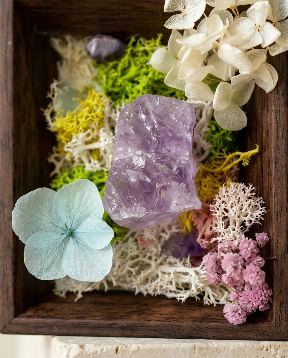 Close-up of an amethyst cluster in a dark wood frame with moss, hydrangea and dried flowers