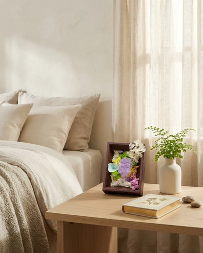 Amethyst framed landscape on a bedroom nightstand beside a plant and a book