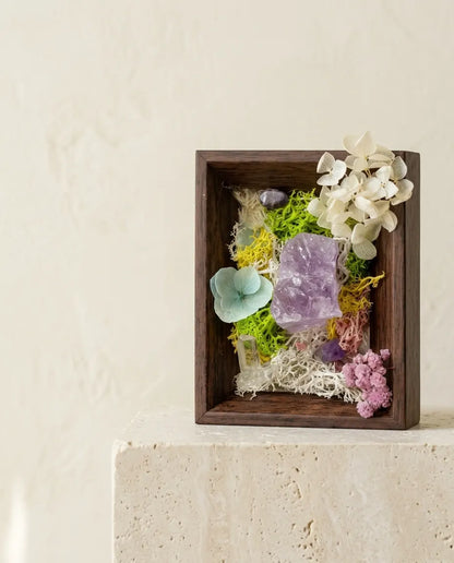 Amethyst, moss and dried flowers in a dark wood frame on a stone plinth