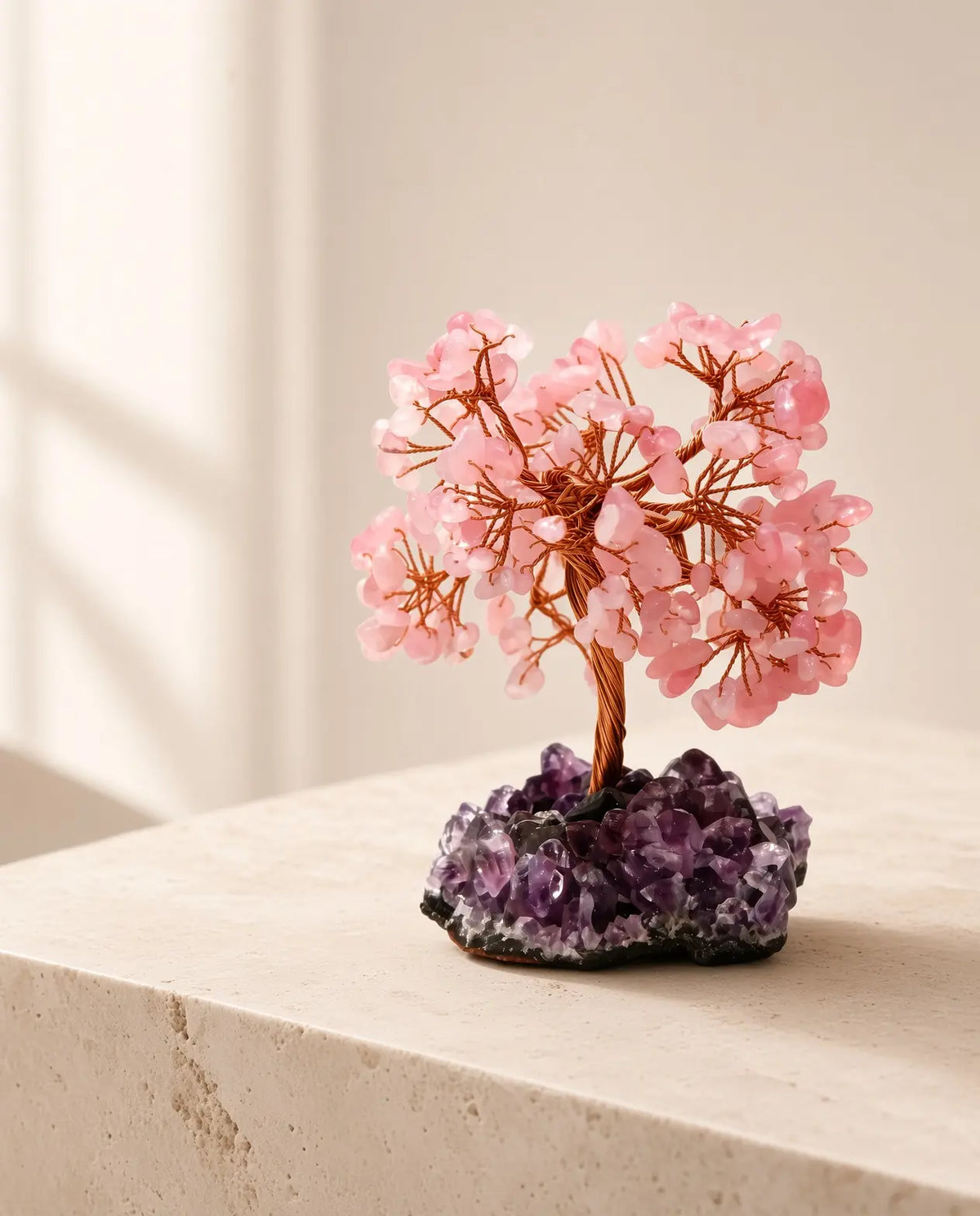 Handmade rose quartz crystal tree on an amethyst base in a bright, minimalist interior