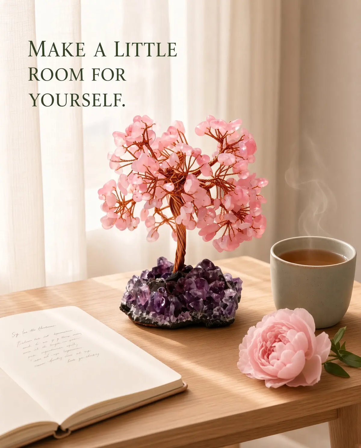 Rose quartz crystal tree styled with tea, journal and a pink flower on a sunlit wooden table