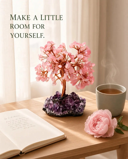 Rose quartz crystal tree styled with tea, journal and a pink flower on a sunlit wooden table