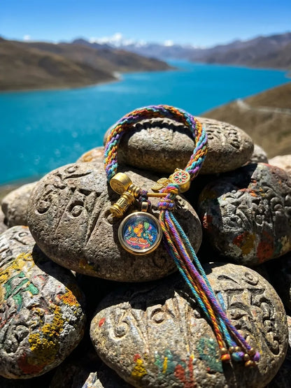 Thangka bracelet on carved mani stones beside a turquoise mountain lake