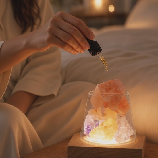 Woman adding essential oil to a glowing amethyst and Himalayan salt aroma lamp on a bedroom nightstand, creating a quiet evening ritual of earth, light, and scent